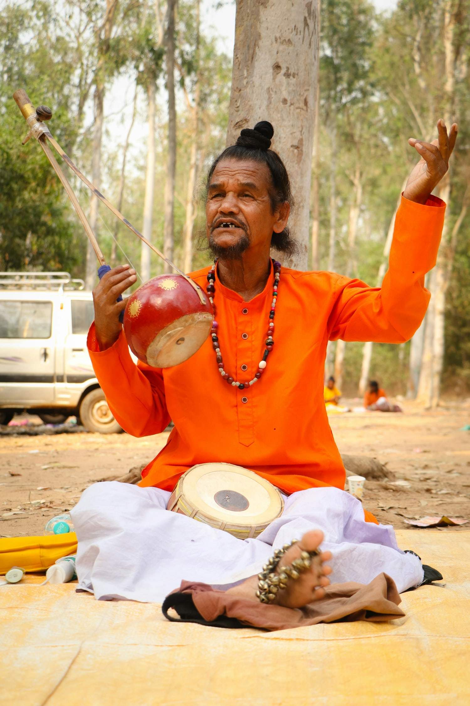A Baul musician in saffron raising an ektara as he sings